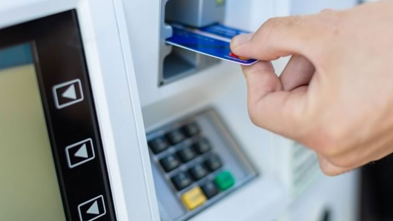A hand fitting a credit card into a gas pump card reader.