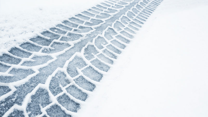 Tire tracks are imprinted on a snowy road.